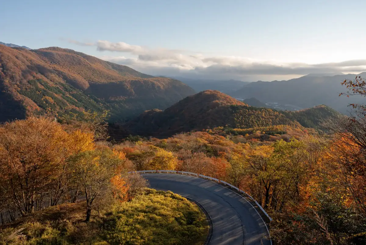 The Irohazaka road curving through autumn forest with mountains behind