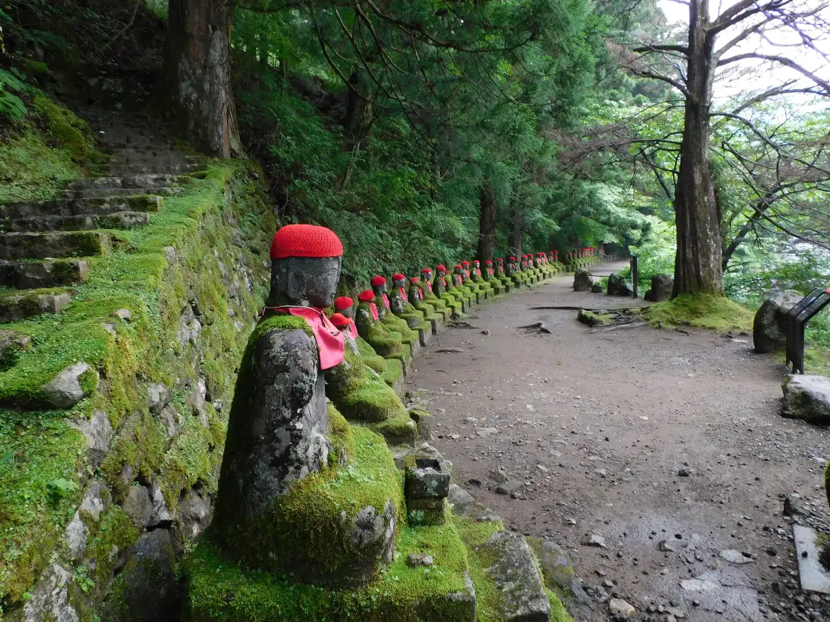 A row of moss-covered stone Jizo statues with red caps along a forest path at Kanmangafuchi